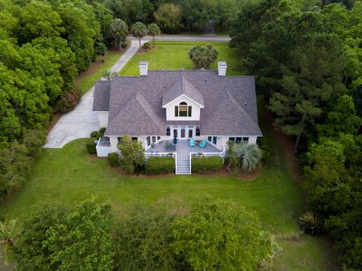 Aerial view of large home with new roof on wooded grassy property